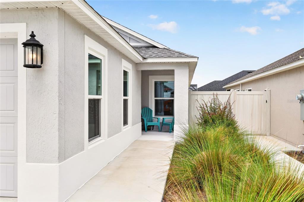 A concrete walkway leads to a covered entryway with two chairs beside a light-colored house — 6125 ROSEN COURT, THE VILLAGES, FL