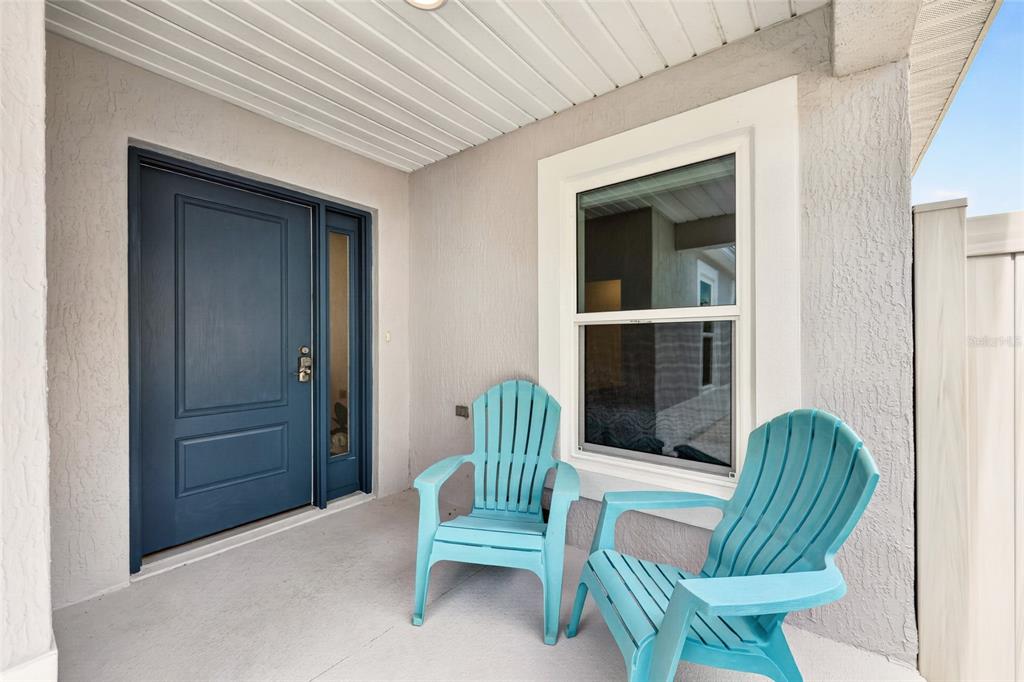 A covered porch features a blue front door, a window, and two light blue Adirondack chairs — 6125 ROSEN COURT, THE VILLAGES, FL