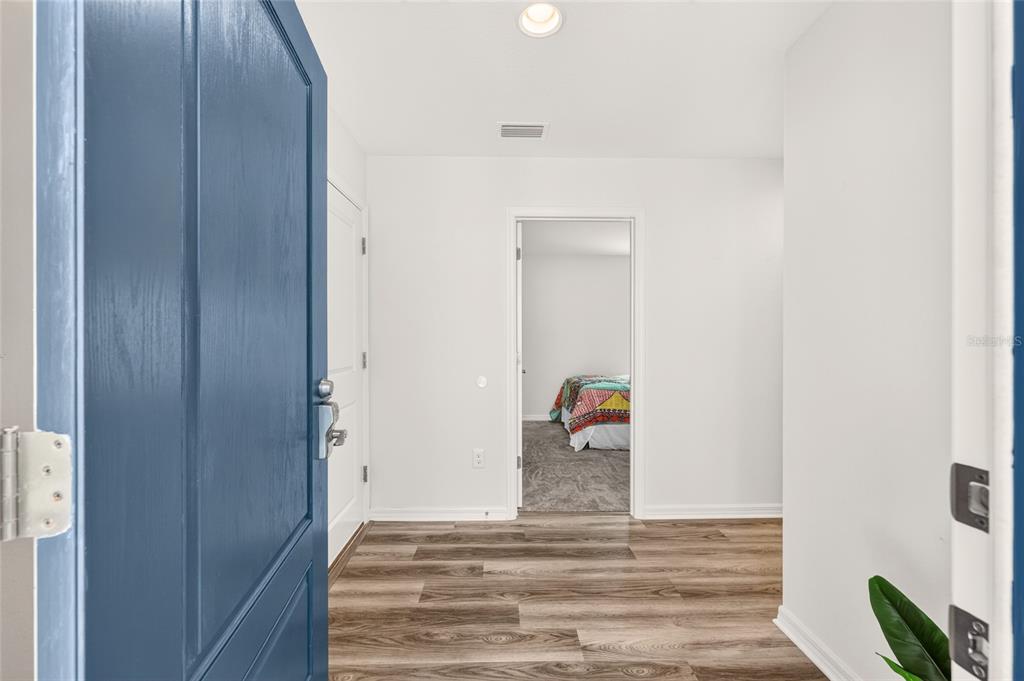 An entryway with wood-look flooring leads to a bedroom visible through an open doorway — 6125 ROSEN COURT, THE VILLAGES, FL