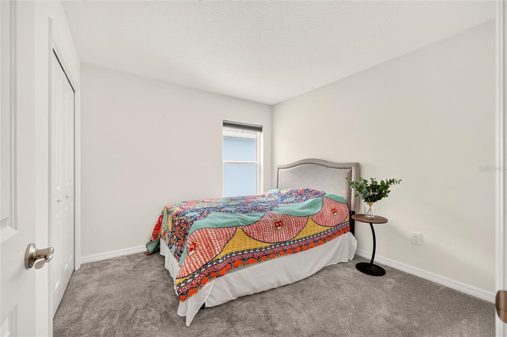 A bedroom features gray carpeting, white walls, a bed with a colorful quilt, and a window — 6125 ROSEN COURT, THE VILLAGES, FL