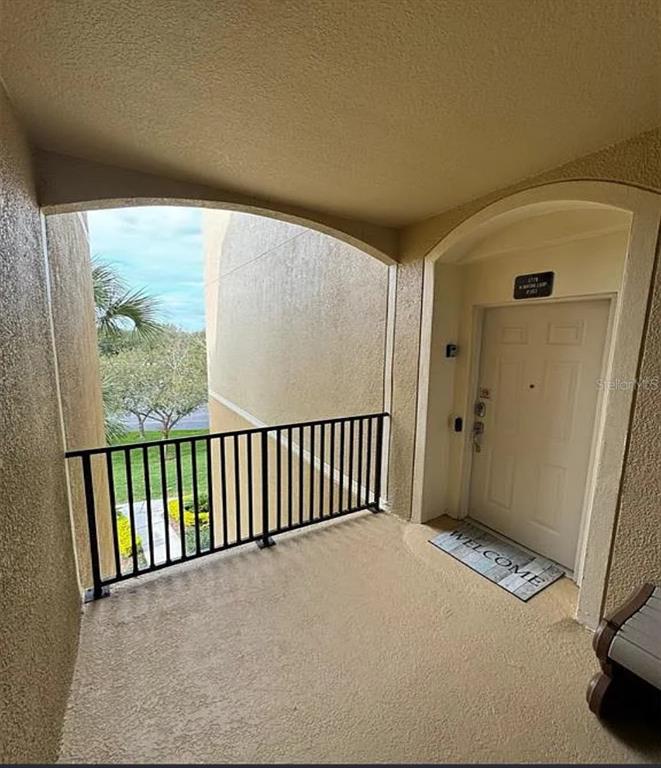 An elevated apartment balcony features a black metal railing, beige stucco walls, and a door — 2778 ALMATON LOOP UNIT 303, KISSIMMEE, FL