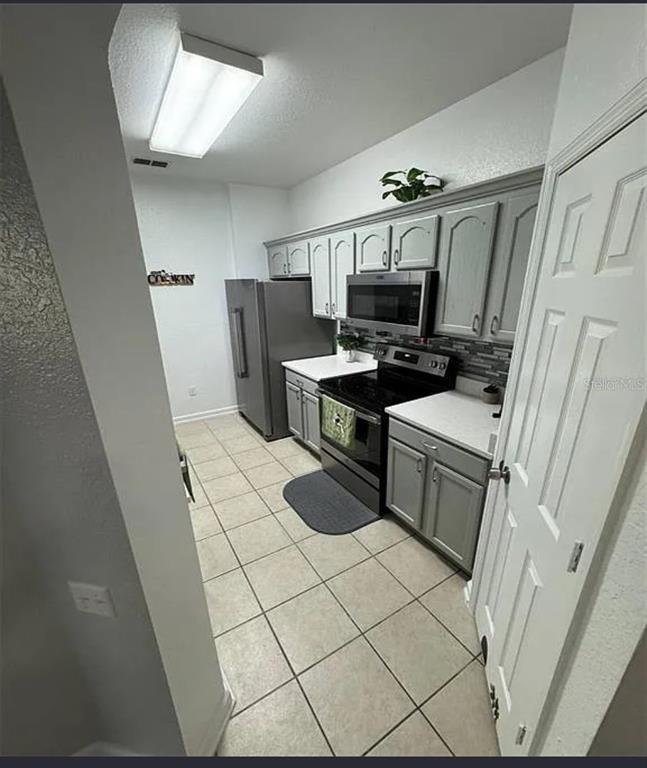 A kitchen features gray cabinets, stainless steel appliances, white countertops, and light-colored tile flooring — 2778 ALMATON LOOP UNIT 303, KISSIMMEE, FL