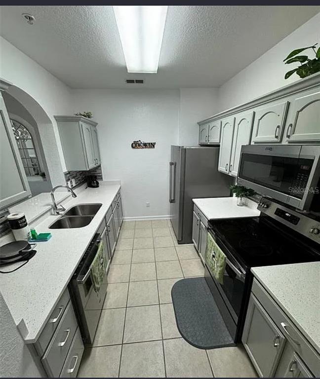 A galley kitchen features light gray cabinets, white countertops, stainless steel appliances, and tile flooring — 2778 ALMATON LOOP UNIT 303, KISSIMMEE, FL
