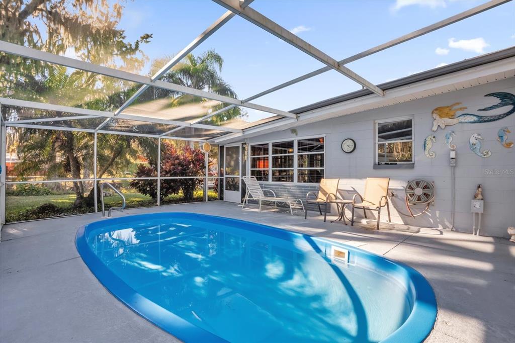 A screened-in patio features a blue oval swimming pool and outdoor furniture against a house — 8150 SPRING DRIVE, YALAHA, FL