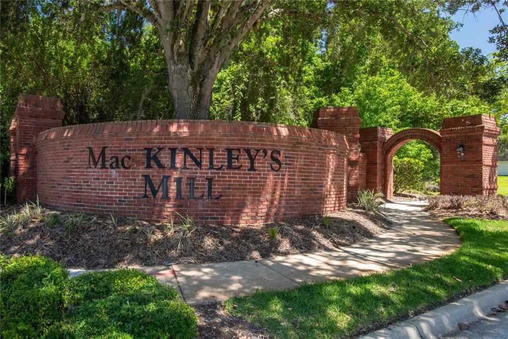 A curved brick wall with the text Mac Kinley's Mill stands beside a brick arched walkway — 1045 ABBOTSFORD COURT, OVIEDO, FL