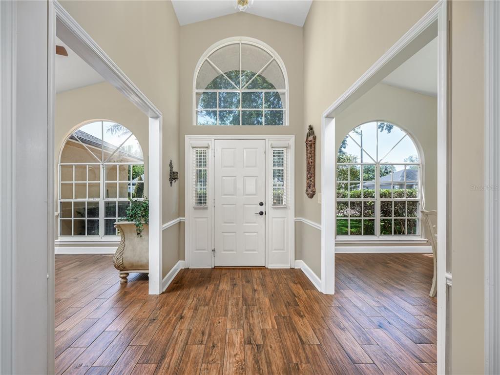 A foyer with wood-look tile flooring, a white front door, and arched windows — 1045 ABBOTSFORD COURT, OVIEDO, FL