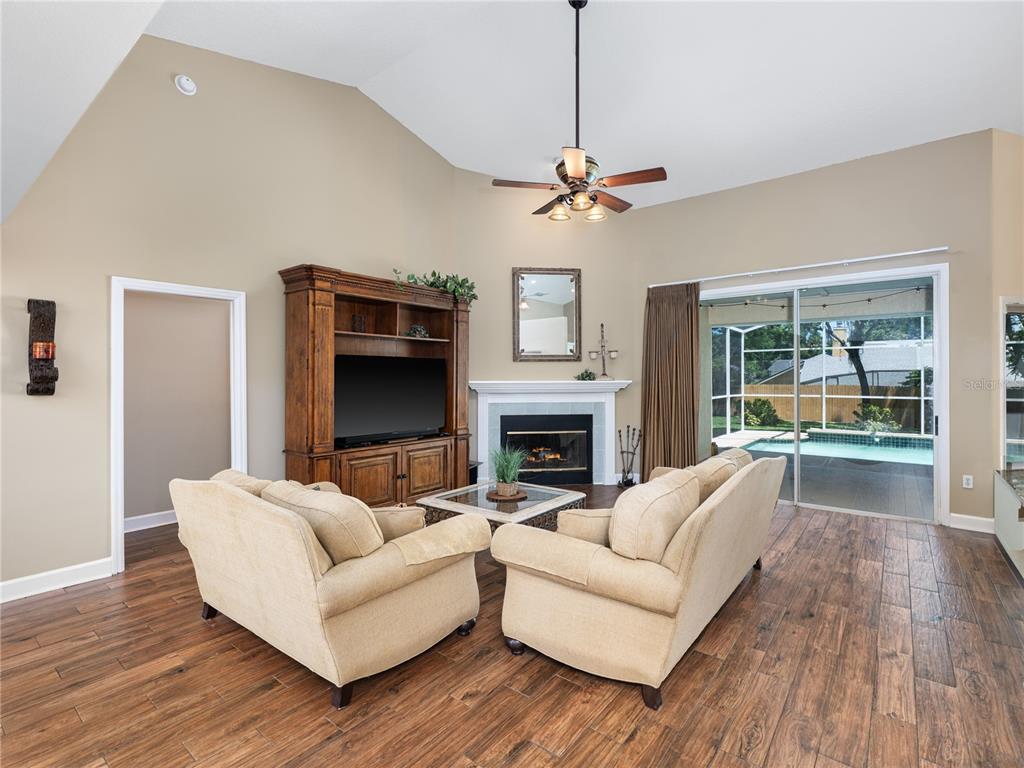 A living room features a fireplace, entertainment center, two beige sofas, and a pool view — 1045 ABBOTSFORD COURT, OVIEDO, FL