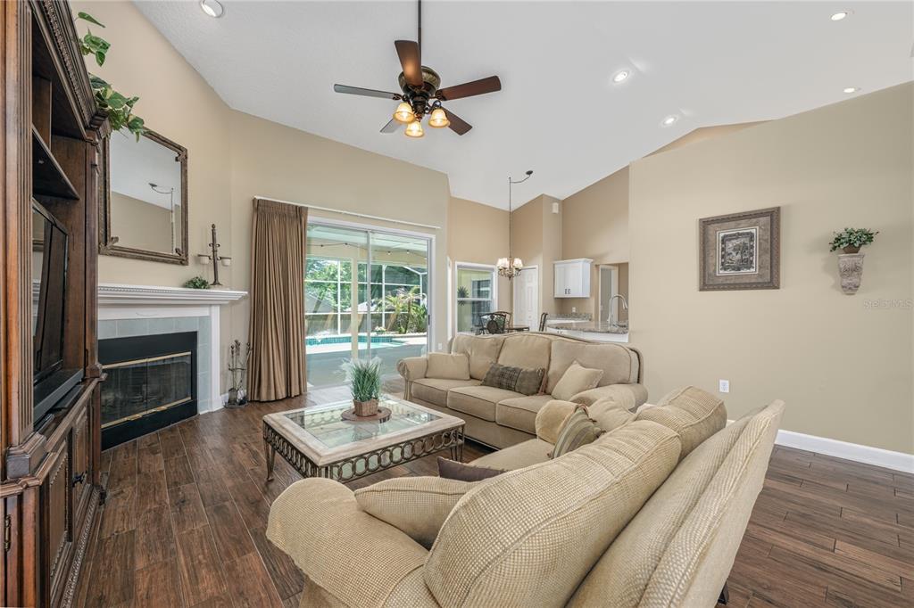 A living room features a fireplace, beige sofas, wood-look tile flooring, and a sliding glass door — 1045 ABBOTSFORD COURT, OVIEDO, FL