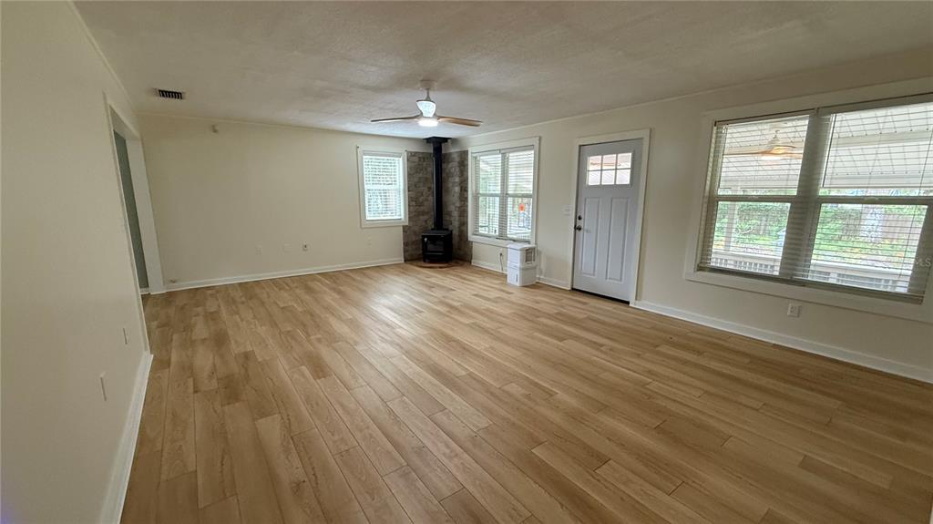 A living room with light wood-look flooring, a wood-burning stove, and a white exterior door — 1520 BADEN POWELL ROAD, HAWTHORNE, FL