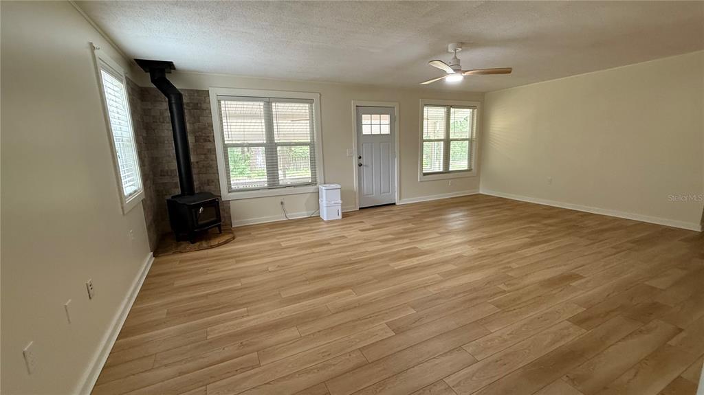 A living room features light wood-look flooring, a wood-burning stove, and a ceiling fan — 1520 BADEN POWELL ROAD, HAWTHORNE, FL