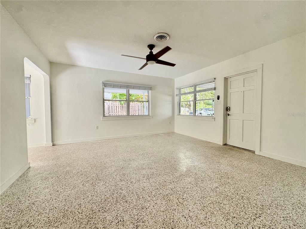 A bright, empty room features white walls, a ceiling fan, and speckled terrazzo flooring — 4722 STEVENS DRIVE, SARASOTA, FL