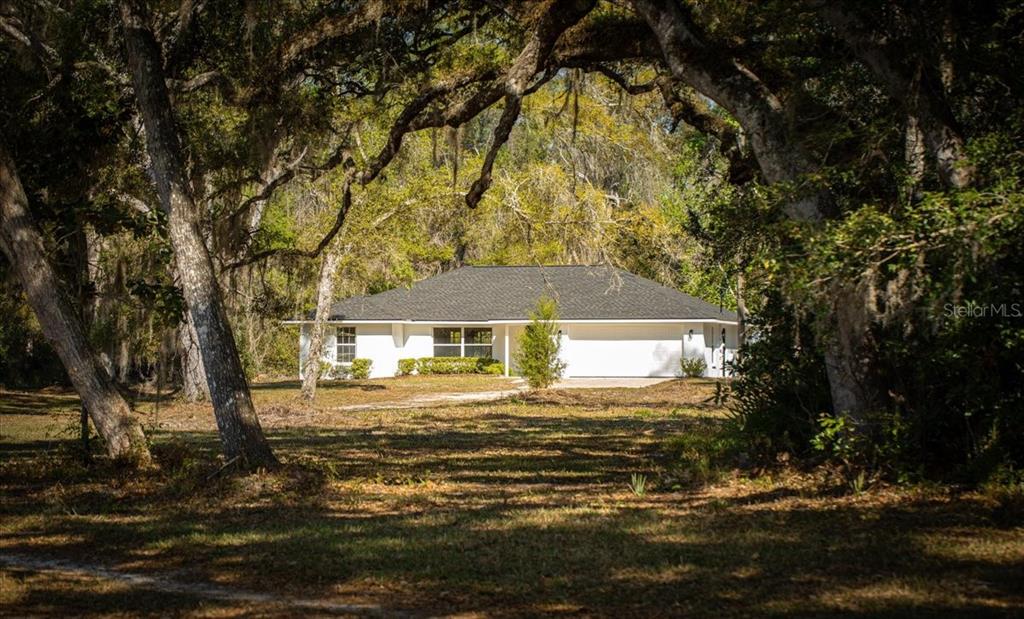 A white single-story house with a dark roof sits behind large trees in a yard — 957 NE 354TH AVENUE, OLD TOWN, FL