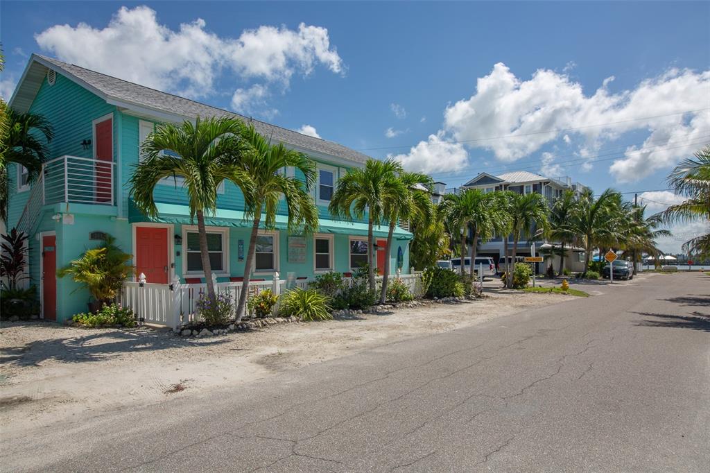 A two-story turquoise house with palm trees and a white fence sits along a street — 308 2ND STREET N UNIT 201, BRADENTON BEACH, FL