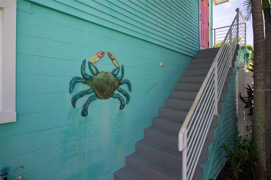 A teal exterior wall features a decorative metal crab and stairs leading to a pink door — 308 2ND STREET N UNIT 201, BRADENTON BEACH, FL