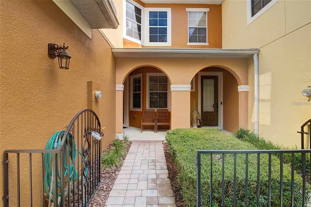 A paved walkway leads to a covered entryway with two arched openings and wooden chairs — 2680 SWEET MAGNOLIA PL, OVIEDO, FL