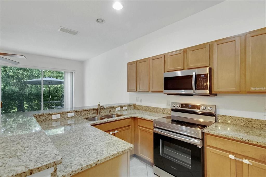 A kitchen features light wood cabinets, granite countertops, and stainless steel appliances — 2680 SWEET MAGNOLIA PL, OVIEDO, FL