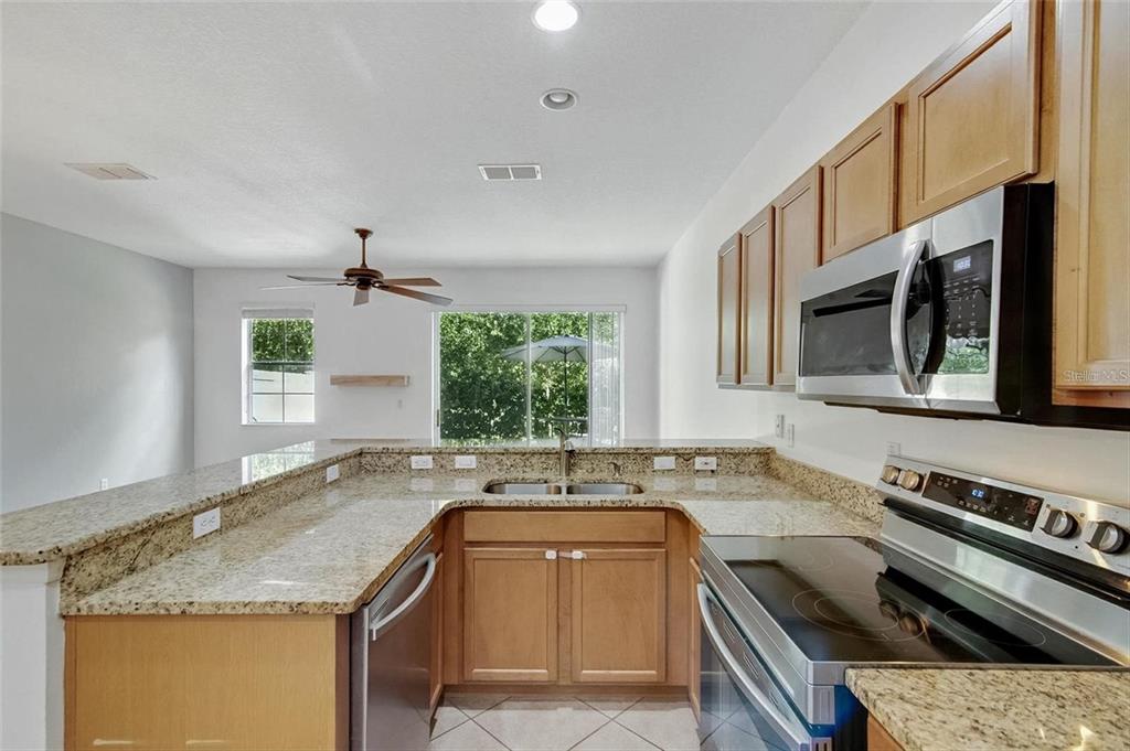 A kitchen with granite countertops, light wood cabinets, and stainless steel appliances overlooks a living area — 2680 SWEET MAGNOLIA PL, OVIEDO, FL