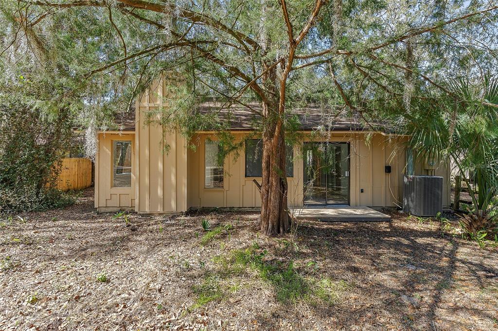 The exterior of a tan, single-story house features a chimney, sliding glass doors, and trees — 38 SNARESBROOK COURT, ORMOND BEACH, FL