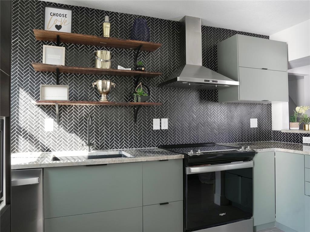 A kitchen features sage green cabinets, a black herringbone tile backsplash, and open wooden shelving — 121-123 N HOLLYWOOD AVENUE, DAYTONA BEACH, FL