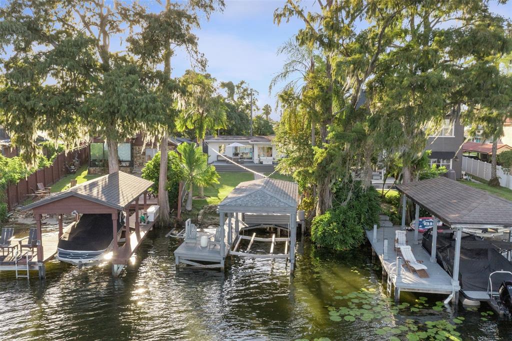 A waterfront property features three boat docks, a grassy lawn, and a house with trees — 560 OLOLU DRIVE, WINTER PARK, FL