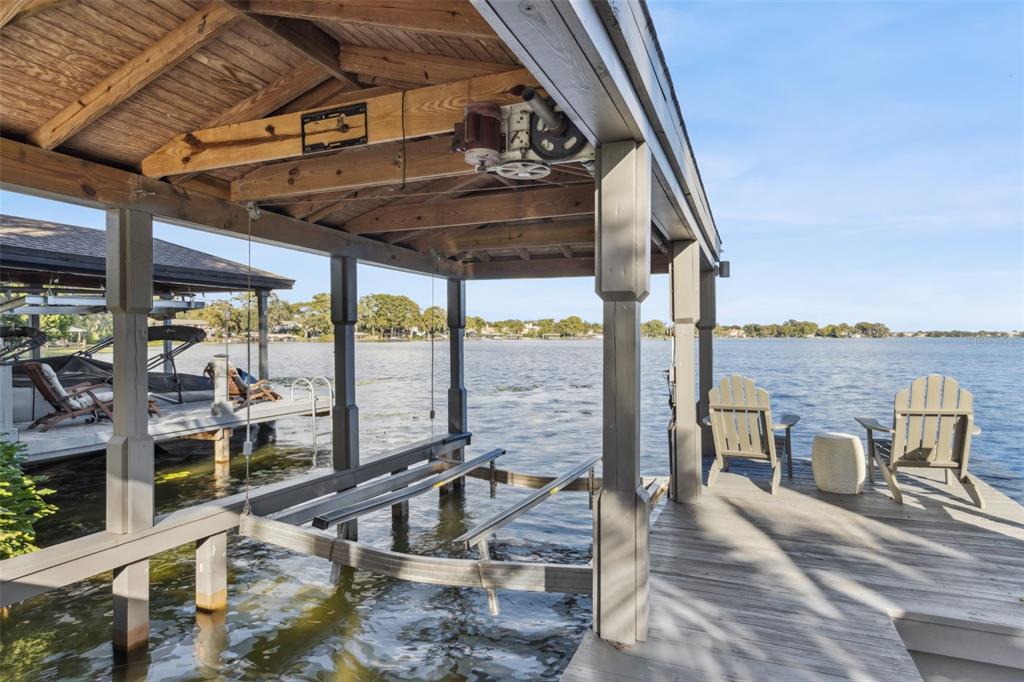 A covered boat lift sits beside a wooden dock with two chairs overlooking a lake — 560 OLOLU DRIVE, WINTER PARK, FL