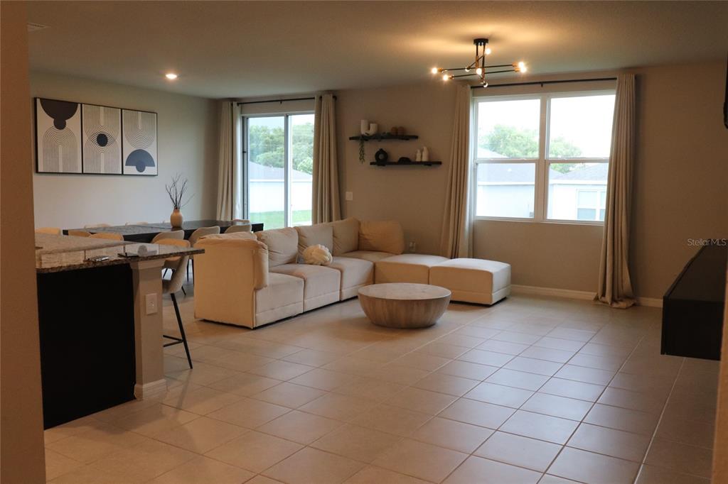 An open-concept living and dining area features tile flooring, a beige sectional, and large windows — 920 CAMBRIDGE DRIVE, WINTER HAVEN, FL