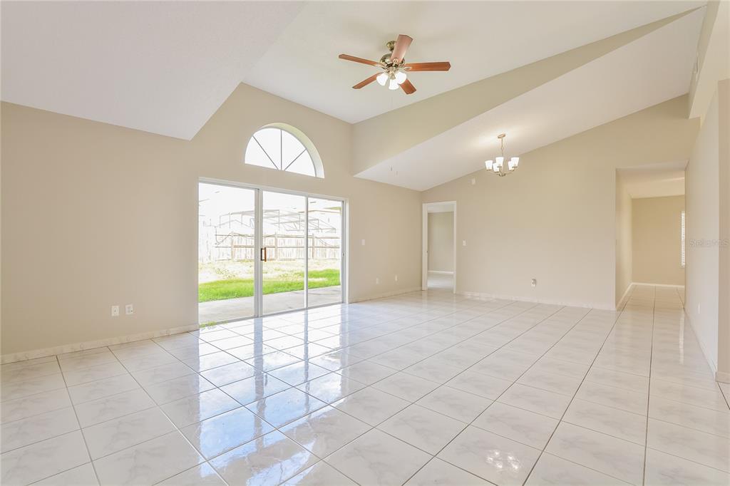 A bright living room features vaulted ceilings, white tile flooring, and sliding glass patio doors — 1515 WOOD VIOLET DRIVE, ORLANDO, FL