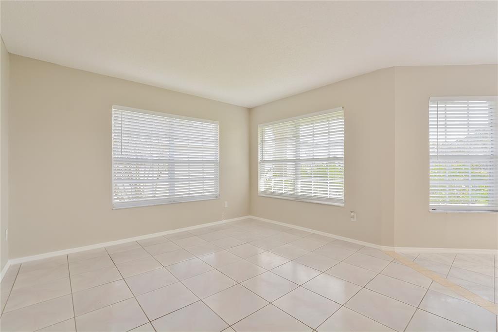 An empty room with light-colored tile flooring, beige walls, and three windows with white blinds — 1515 WOOD VIOLET DRIVE, ORLANDO, FL