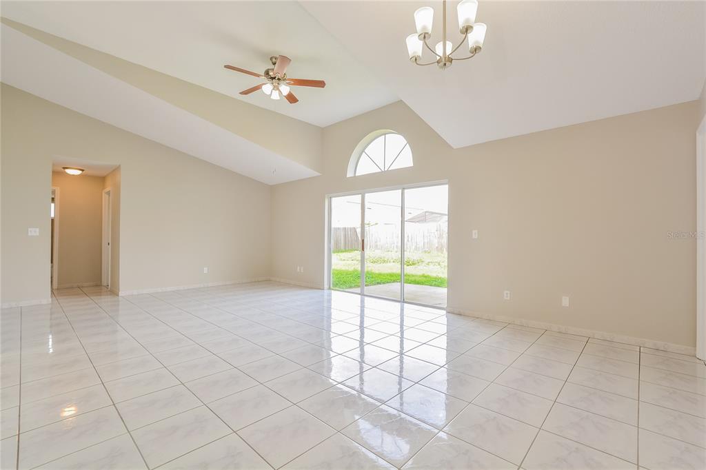 A spacious living room with vaulted ceilings, white tile flooring, and sliding glass patio doors — 1515 WOOD VIOLET DRIVE, ORLANDO, FL