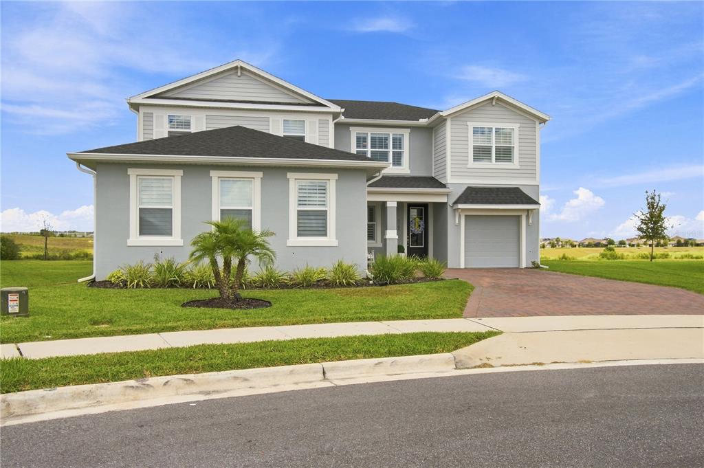 A two-story suburban house with light gray siding, a brick driveway, and two garages — 3168 CANNA LILY PLACE, CLERMONT, FL