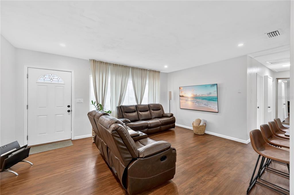 A living room features brown leather sofas, wood-look flooring, and a wall-mounted television — 2010 LEE DRIVE, VALRICO, FL