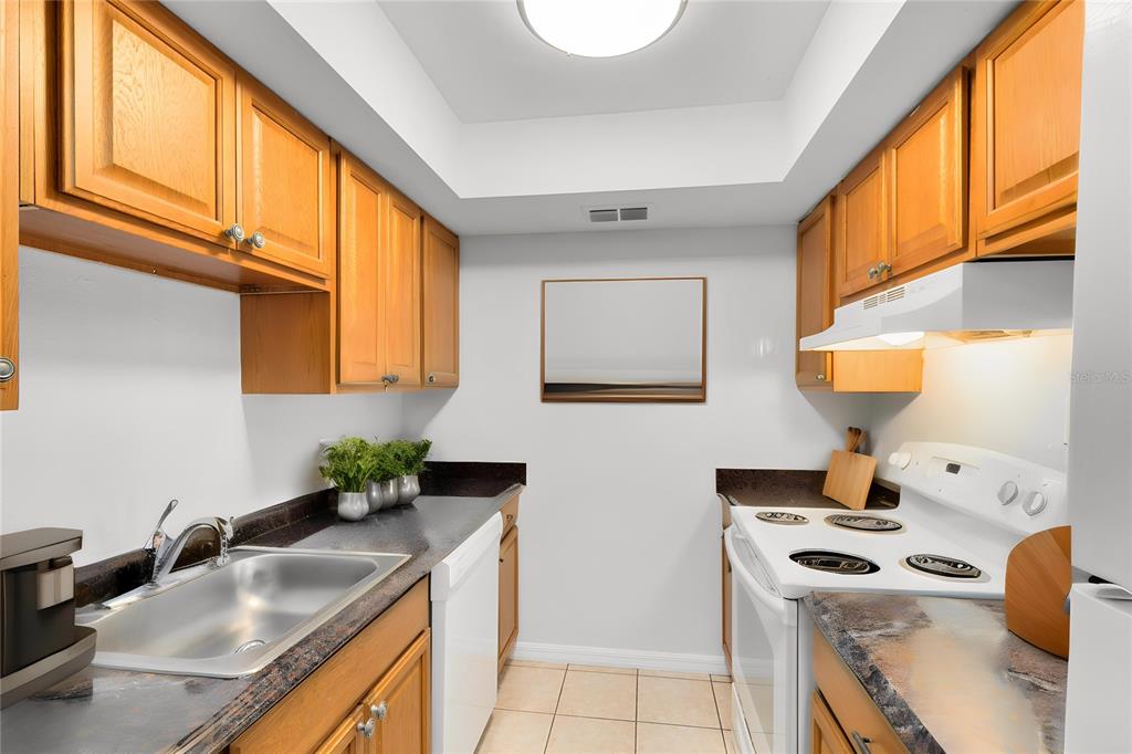 A galley kitchen features light wood cabinets, dark countertops, white appliances, and tiled flooring — 1040 S BUENA VISTA DRIVE UNIT 1040, LAKE ALFRED, FL