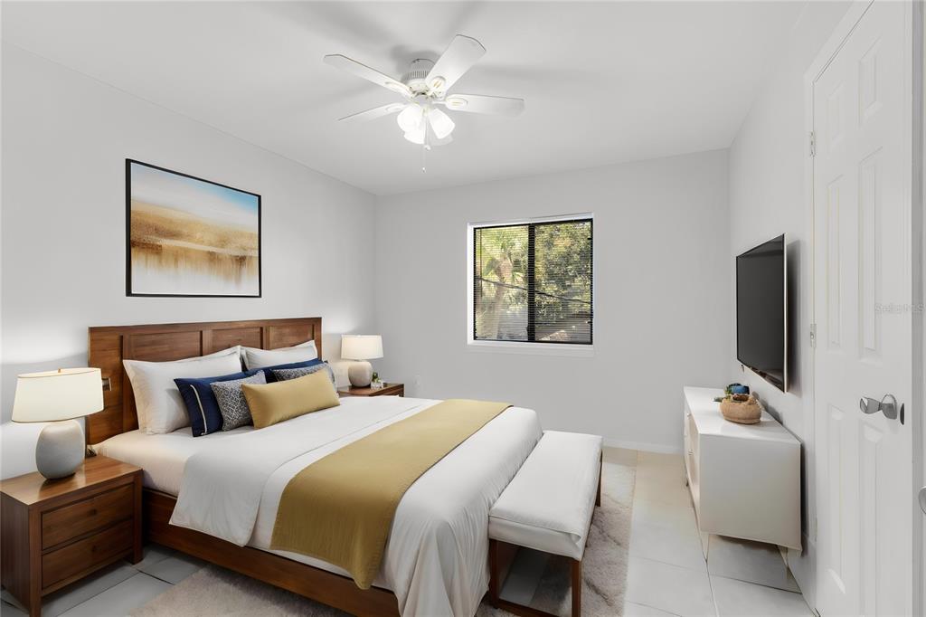 A bedroom features a wooden bed frame, white bedding, a ceiling fan, and a wall-mounted television — 1040 S BUENA VISTA DRIVE UNIT 1040, LAKE ALFRED, FL