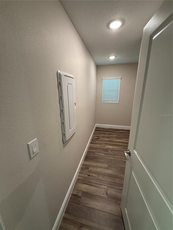A small room features wood-look flooring, light-colored walls, a window with blinds, and an electrical panel — 9924 ANNUNCIATION DRIVE, WESLEY CHAPEL, FL