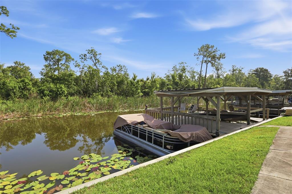 A pontoon boat is docked at a wooden pier on a canal with lily pads — 26638 E COVE DRIVE, TAVARES, FL