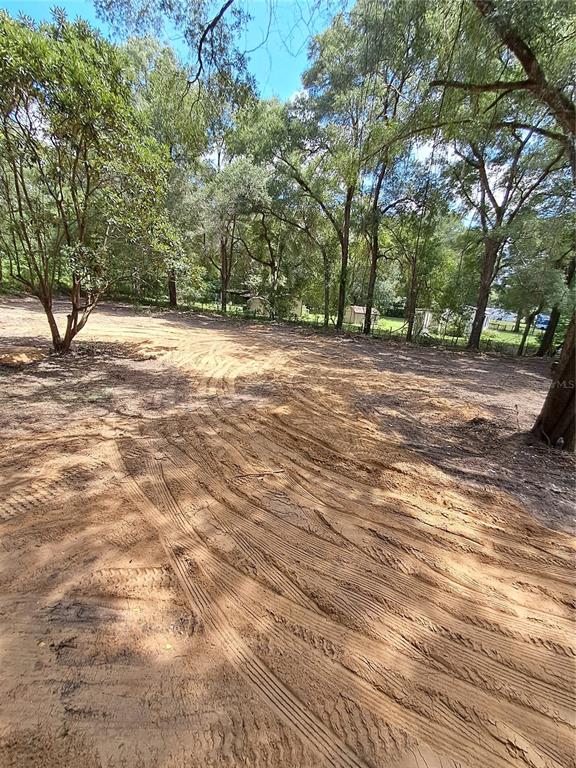 A dirt lot with tire tracks is surrounded by mature trees and distant small structures — 5601 NW 71ST STREET, OCALA, FL