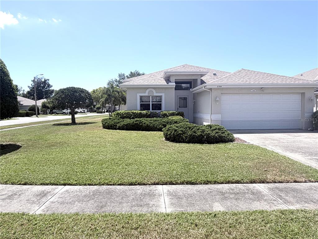 A single-story suburban house with a beige exterior, a two-car garage, and a manicured lawn — 2784 ALEXANDER DRIVE, CLEARWATER, FL