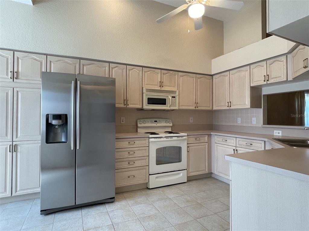 A kitchen features light-colored cabinets, stainless steel appliances, a white stove, and tile flooring — 2784 ALEXANDER DRIVE, CLEARWATER, FL