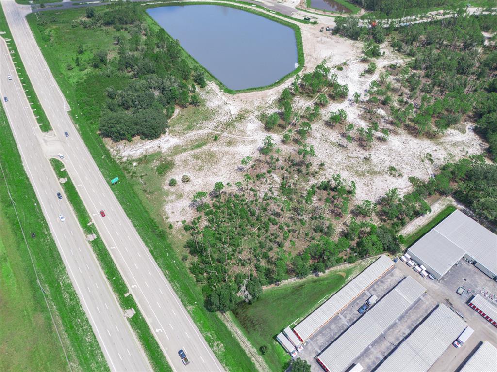 An aerial view shows a vacant lot next to a highway, a pond, and warehouses — US-27, LAKE WALES, FL