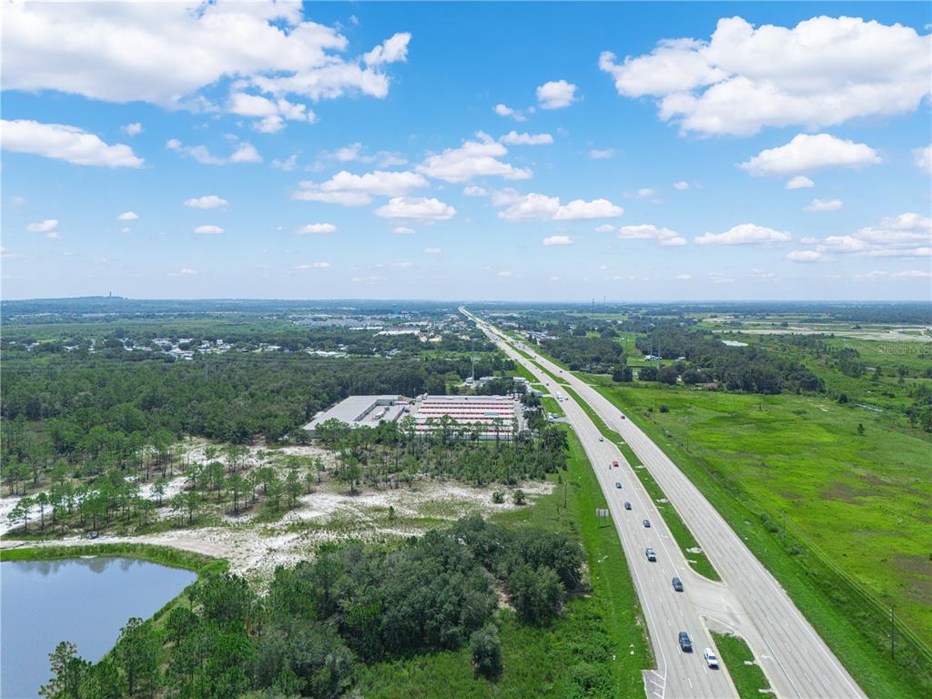 An aerial view shows a highway running past a large storage facility and a pond — US-27, LAKE WALES, FL
