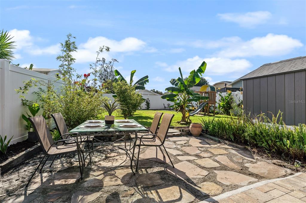 A stone patio features a glass-topped dining table and chairs in a fenced backyard — 145 MAYFAIR COURT UNIT 145, SANFORD, FL