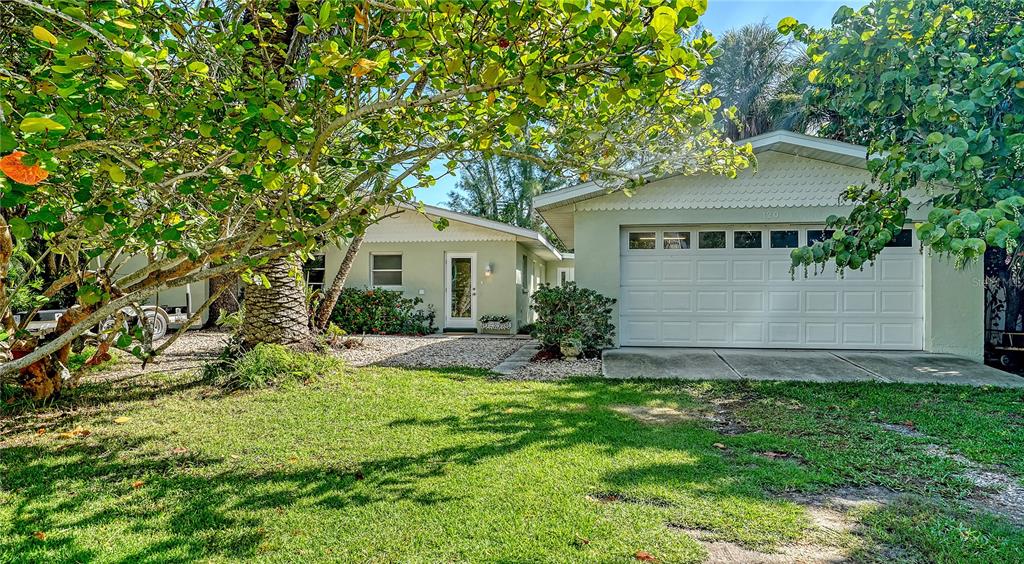 A light green house with a white garage door and a gravel driveway under trees — 120 HAMMOCK ROAD, ANNA MARIA, FL