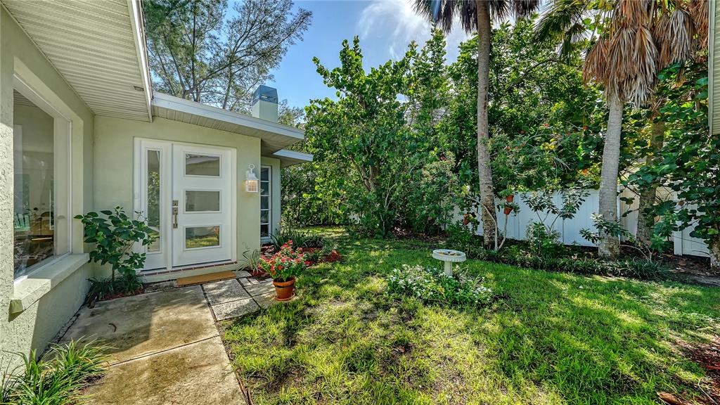 A white front door with glass panels sits beside a small garden and lawn area — 120 HAMMOCK ROAD, ANNA MARIA, FL