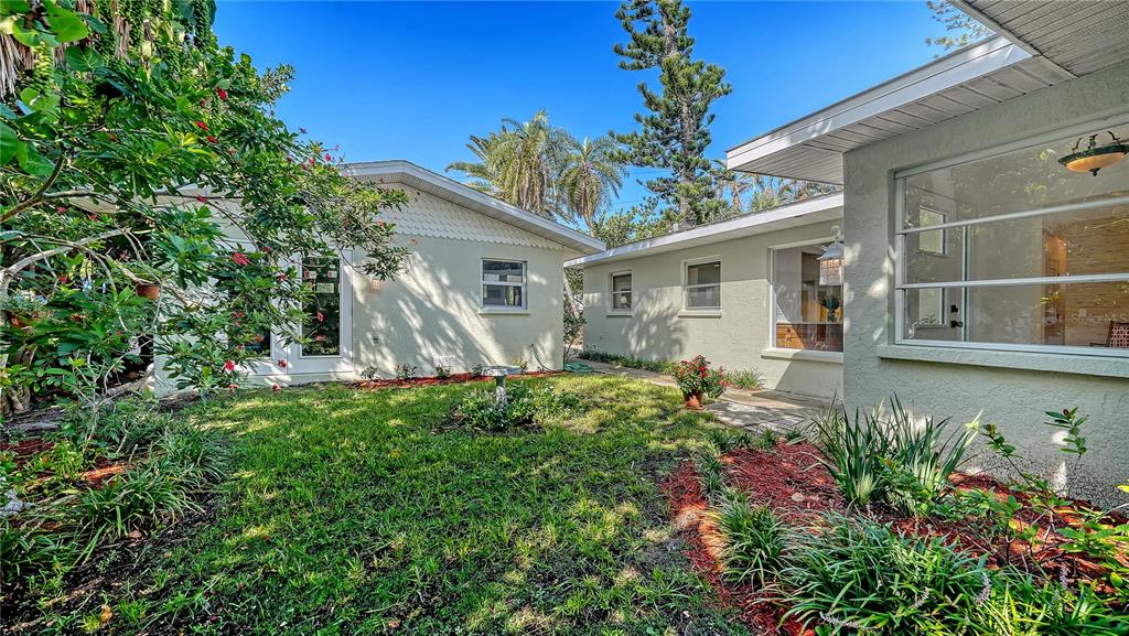 A grassy backyard features a light-colored house with a patio and lush landscaping — 120 HAMMOCK ROAD, ANNA MARIA, FL