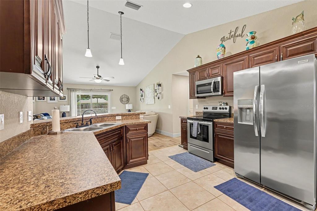 A kitchen with dark wood cabinets, granite countertops, stainless steel appliances, and tile flooring — 4 MALAUKA RADIAL PASS, OCKLAWAHA, FL