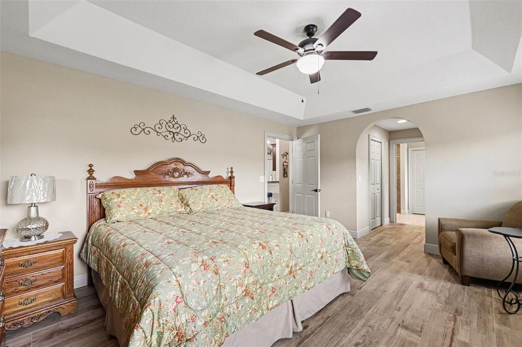 A bedroom features a wooden bed frame, floral bedding, a ceiling fan, and wood-look flooring — 4 MALAUKA RADIAL PASS, OCKLAWAHA, FL