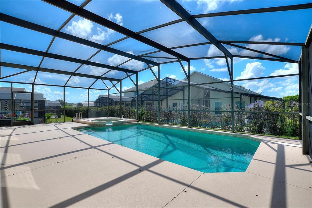A screened-in swimming pool and hot tub on a concrete patio under a blue sky — 16616 PALM SPRING DRIVE, CLERMONT, FL