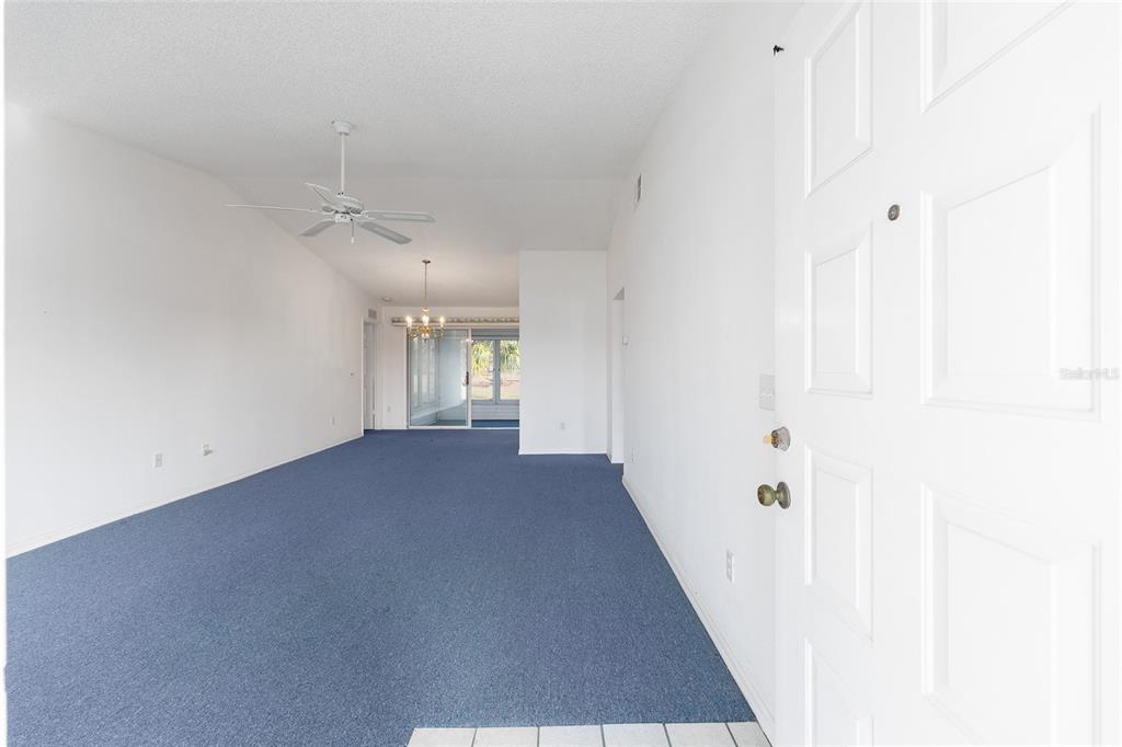 An interior view of a living room with blue carpeting, white walls, and a ceiling fan — 6511 SW 85TH STREET, OCALA, FL