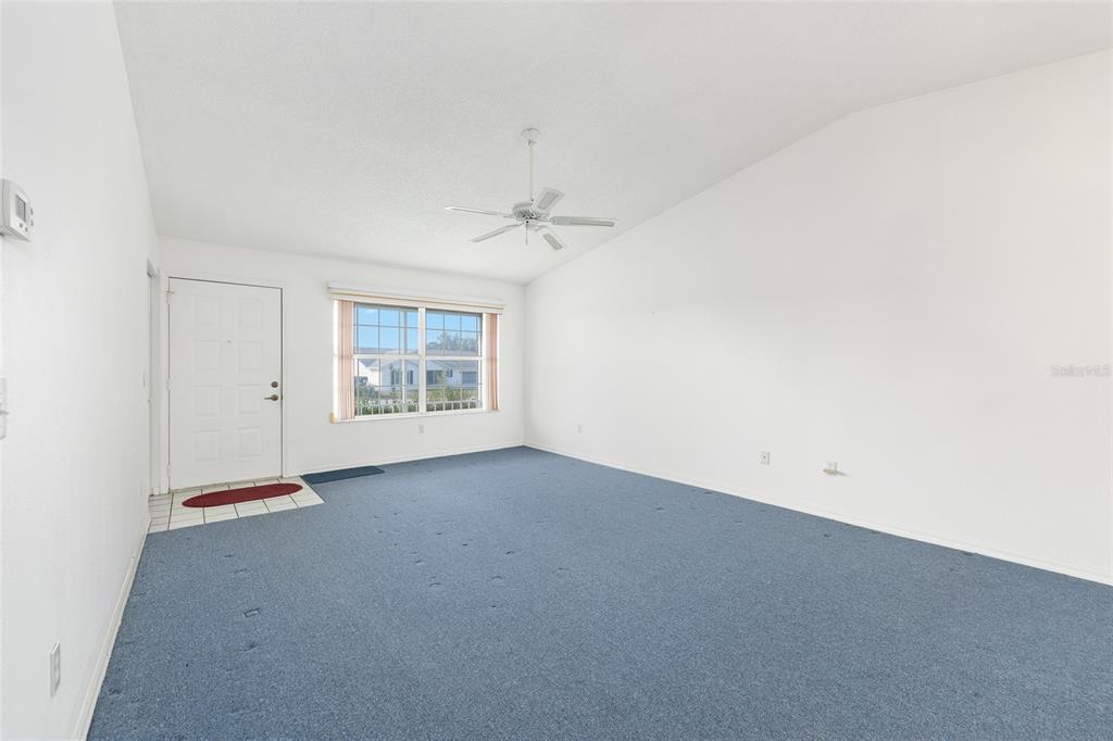 An empty living room features blue carpeting, white walls, a ceiling fan, and a door — 6511 SW 85TH STREET, OCALA, FL