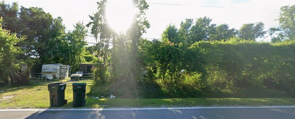 A grassy, overgrown lot features a parked camper and two trash bins near a road — 824 N 6TH STREET, ORLANDO, FL